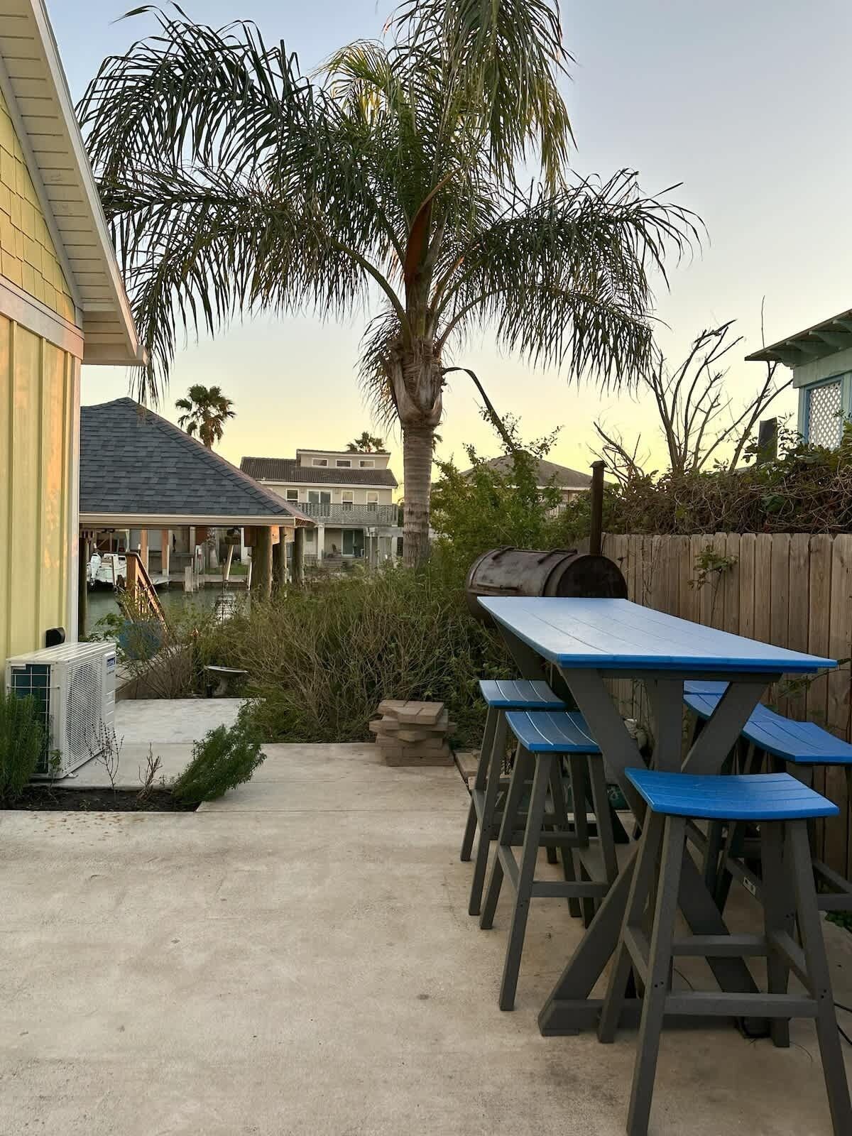 A patio area with a concrete floor, a wooden fence, and a blue table with benches.