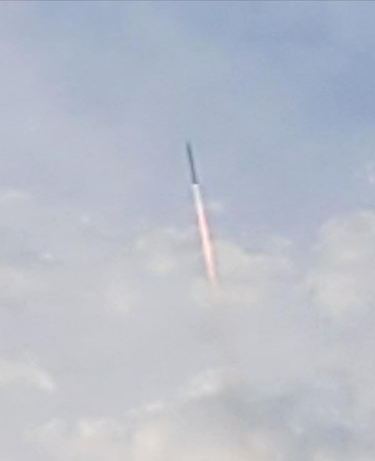 A rocket launch with a visible flame trail against a cloudy sky.