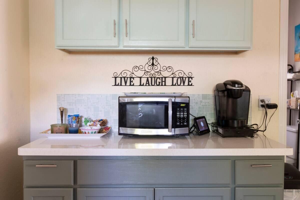 A kitchen with a microwave, coffee maker, and a wall sign that says 'LIVE LAUGH LOVE'.