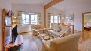 A spacious living room with a wooden ceiling, a television on a stand, two sofas, a coffee table, and a dining area with a table and chairs. - Bright Vicky Apartment With Infrared Sauna (Wildschönau)