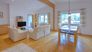 A spacious living area with a wooden ceiling, a sofa, a TV, and a dining table with chairs. - Bright Vicky Apartment With Infrared Sauna (Wildschönau)
