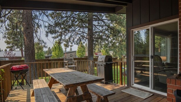 An outdoor deck with a wooden picnic table and benches, a barbecue grill, and a sliding glass door leading to a patio area. - Bluebird Day - Brooks House, Experience comfort in the spacious 3200 sqft, Hot tub, Pet friendly! (Bend)