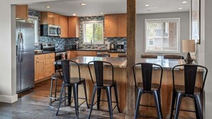 A modern kitchen with a central island, bar stools, and a stainless steel refrigerator. - Bluebird Day - Brooks House, Experience comfort in the spacious 3200 sqft, Hot tub, Pet friendly! (Bend)