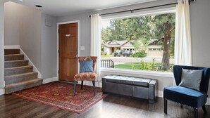 A room with a wooden door, a bench, a chair, and a view of houses through a window. - Bluebird Day - Brooks House, Experience comfort in the spacious 3200 sqft, Hot tub, Pet friendly! (Bend)