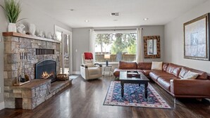 A living room with a stone fireplace, leather sofa, and a large window. - Bluebird Day - Brooks House, Experience comfort in the spacious 3200 sqft, Hot tub, Pet friendly! (Bend)