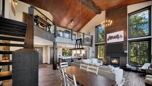 A spacious living area with a large wooden dining table, a fireplace, and a view of the outdoors. - Whispering Woods Peak.  Come see the views? (Lead)