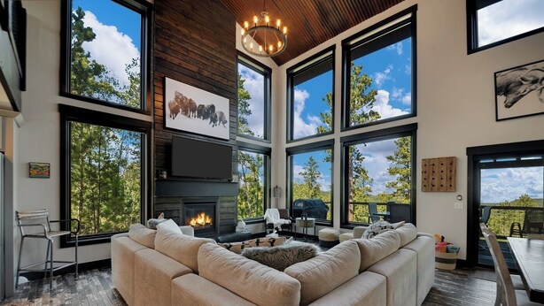 A spacious living room with a large sectional sofa, a fireplace, and large windows offering views of the outdoors. - Whispering Woods Peak.  Come see the views? (Lead)