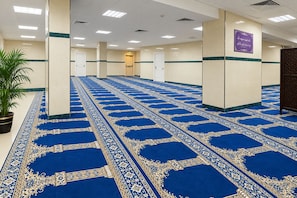 A hallway with a patterned carpet, white walls, and a potted plant. - Jawaher Al Bait 2 Hotel Makkah by oteleia (Makkah)