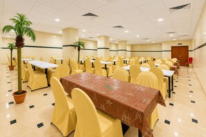 Une salle de conférence avec plusieurs tables et chaises, une plante décorative au centre et une porte au fond.