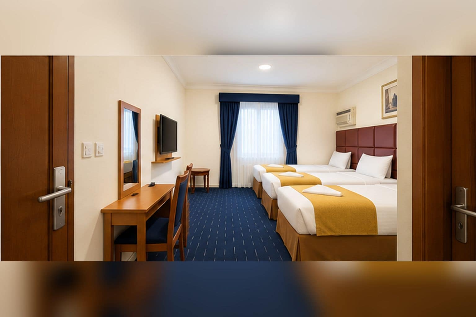 Habitación de hotel con escritorio, televisión y tres camas.