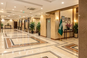 A hotel lobby with a marble floor, elevators, potted plants, and a flag. - Jawaher Al Bait 2 Hotel Makkah by oteleia (Makkah)