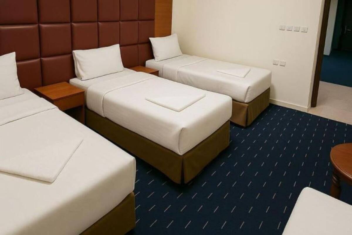 Ein Hotelzimmer mit drei Einzelbetten, einem Holzkopfteil, einem gerahmten Bild an der Wand und einem blau gemusterten Teppich.
