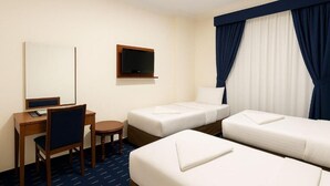 Ein Hotelzimmer mit zwei Einzelbetten, einem Schreibtisch mit Stuhl, einem Fernseher und einem kleinen Tisch.