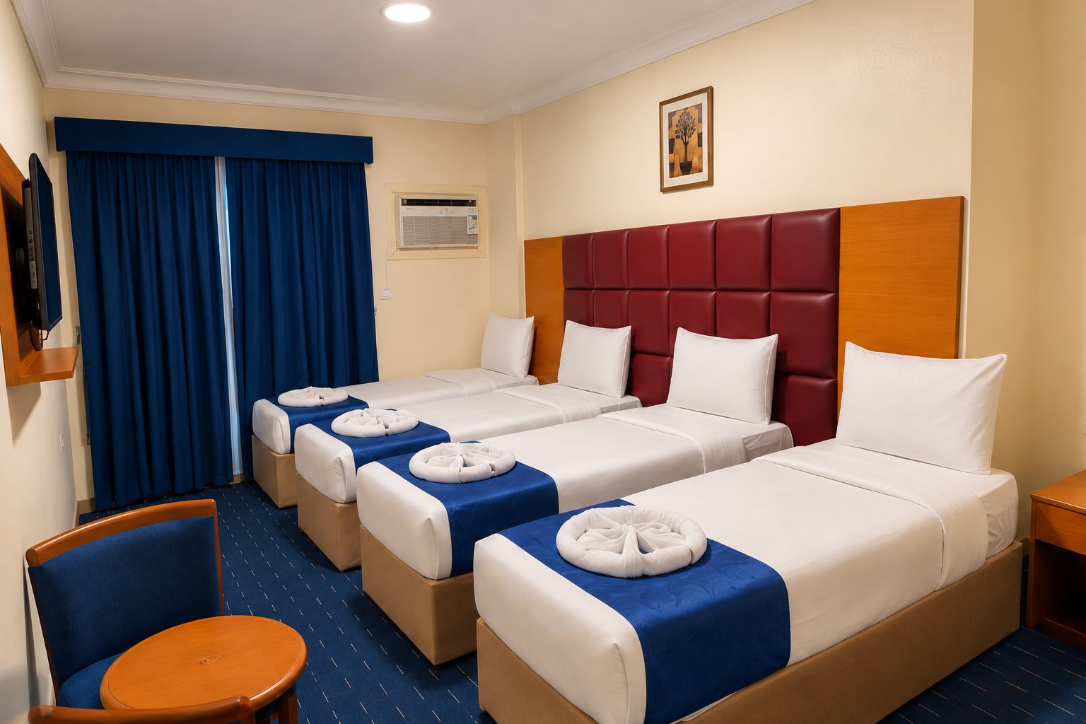 A hotel room with three beds, a television, a window with blue curtains, and a painting on the wall.