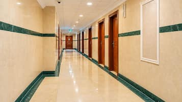 Un pasillo de hotel con piso de mármol, puertas de madera y detalles en verde mármol.