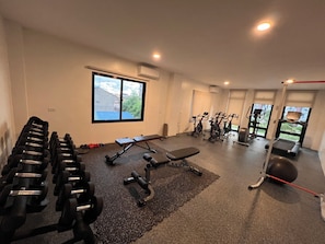 A gym with exercise equipment, a bench, and a window with a view of buildings.