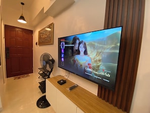 A TV mounted on a wall with a wooden panel, a black fan, and a framed picture above it.