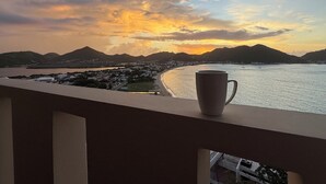 A balcony with a view of a coastal town at sunset. - 5BR Hilltop Villa! Pool & Ocean Views (Sint Maarten)