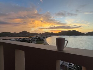 A balcony with a view of a coastal town at sunset. - 5BR Hilltop Villa! Pool & Ocean Views (Sint Maarten)