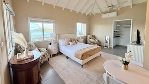 A bedroom with a bed, bedside tables, a chair, a desk, and a view of the sea. - 5BR Hilltop Villa! Pool & Ocean Views (Sint Maarten)