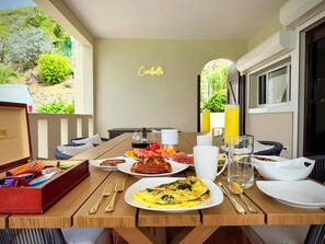 A breakfast table with plates of food, a coffee pot, and a neon sign reading 'Caribelle'. - 5BR Hilltop Villa! Pool & Ocean Views (Sint Maarten)