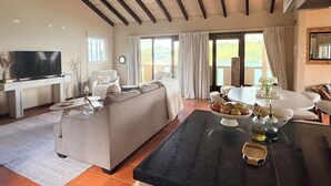 A spacious living room with a large sofa, a dining table with a fruit bowl, a flat-screen TV, and a ceiling fan. - 5BR Hilltop Villa! Pool & Ocean Views (Sint Maarten)