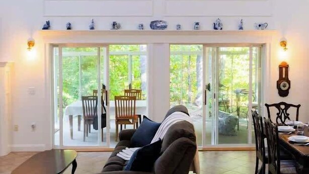 Een ruime woonkamer met een hoge plafond, een groot raam, en een eethoek met een tafel en stoelen.