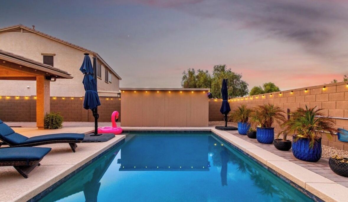 A swimming pool with lounge chairs and umbrellas, surrounded by potted plants and a brick wall.