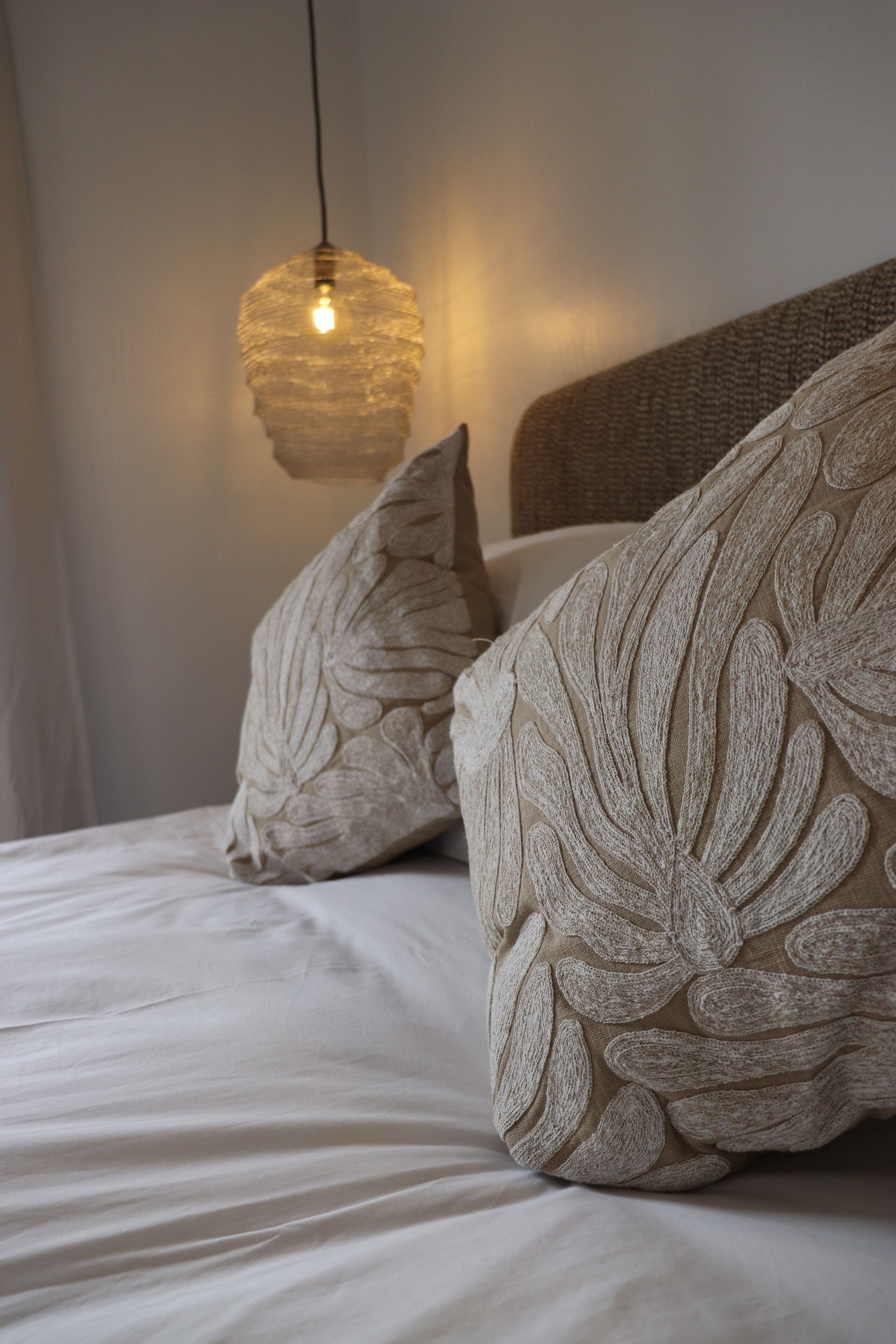 Ein Bett mit weißen Leinentüchern, einem strukturierten Kopfteil und dekorativen Kissen mit Blattmotiven.