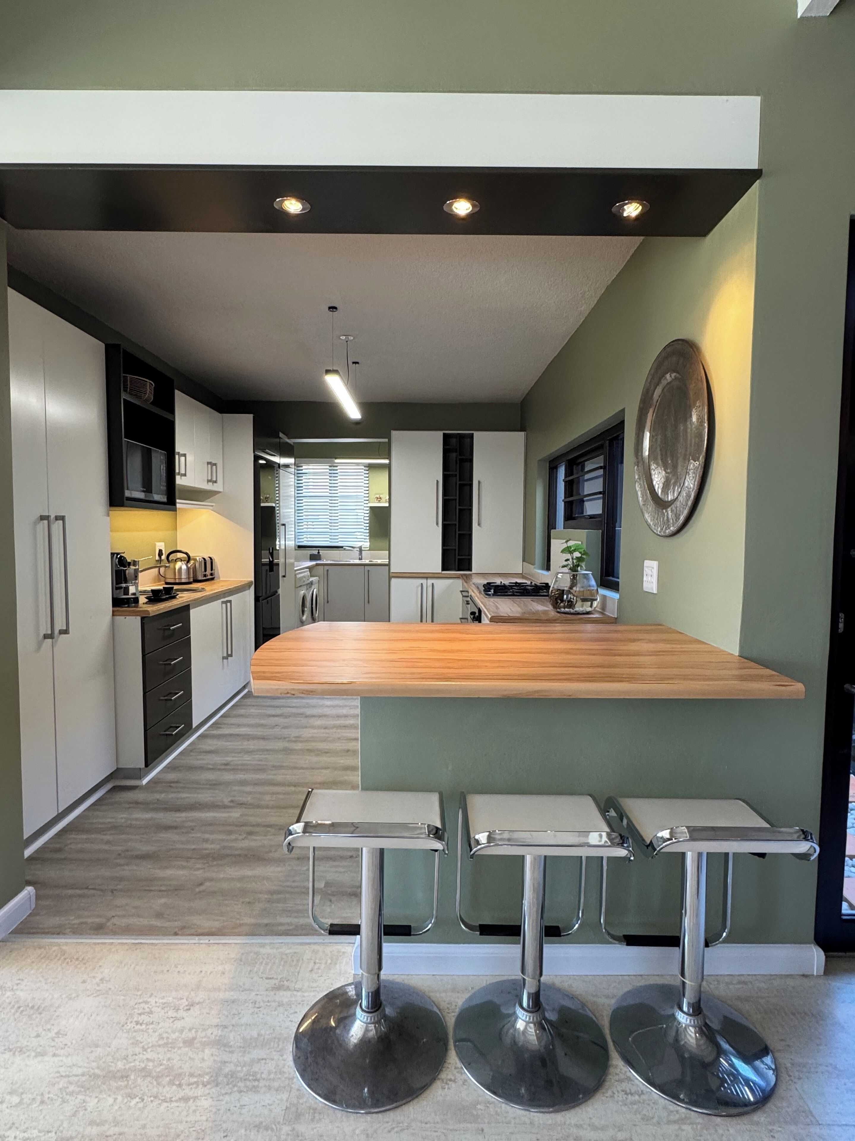 A modern kitchen with a central island, bar stools, and a view into the dining area.