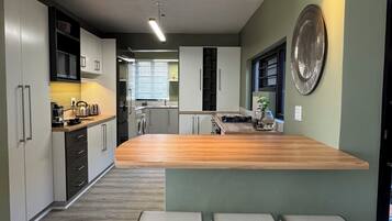 A modern kitchen with a central island, bar stools, and a view into the dining area.