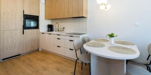 A modern kitchen with wooden cabinets, a built-in oven, a white countertop, and a round dining table with chairs.