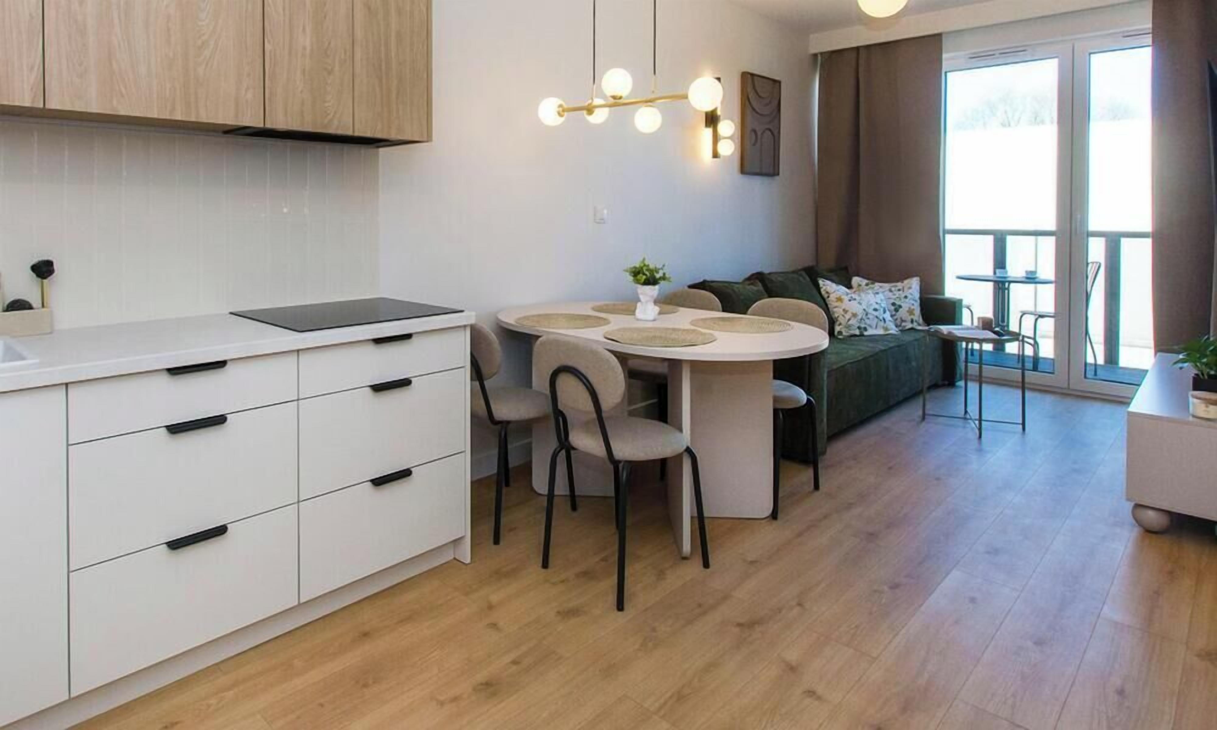Et moderne køkken med hvide skabe, et spisebord med fire stole og en sofa i opholdsstuen.