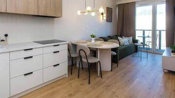 Et moderne køkken med hvide skabe, et spisebord med fire stole og en sofa i opholdsstuen.