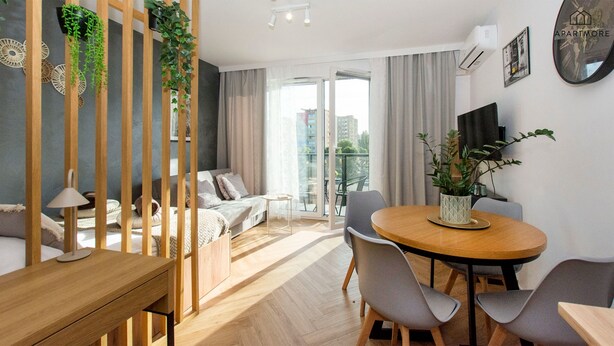 Eine moderne Wohnung mit Esstisch aus Holz, grauen Stühlen, einer Couch und einem Balkon mit Blick auf die Stadt.