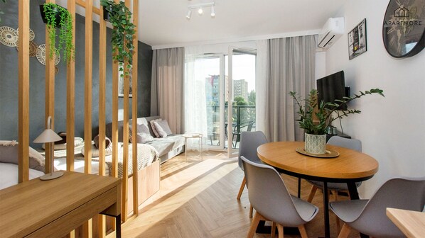 Eine moderne Wohnung mit Esstisch aus Holz, grauen Stühlen, einer Couch und einem Balkon mit Blick auf die Stadt.
