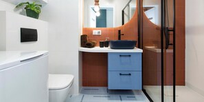 A modern bathroom with a white toilet, a blue cabinet, a black sink, and a glass shower enclosure. - Portovo Residence by Apartmore (Gdańsk)
