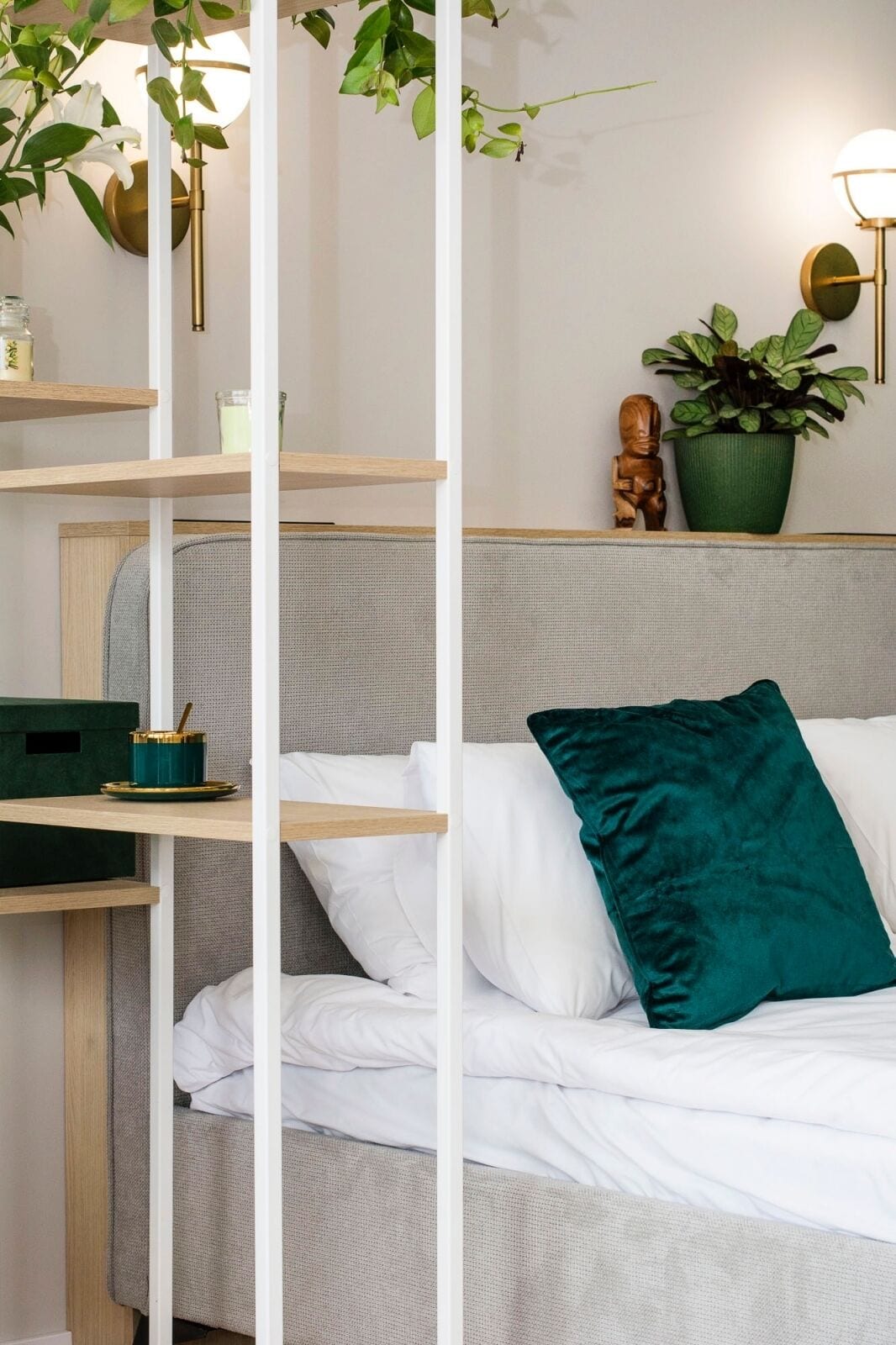 A bed with white bedding, a green pillow, and a green plant on a shelf.