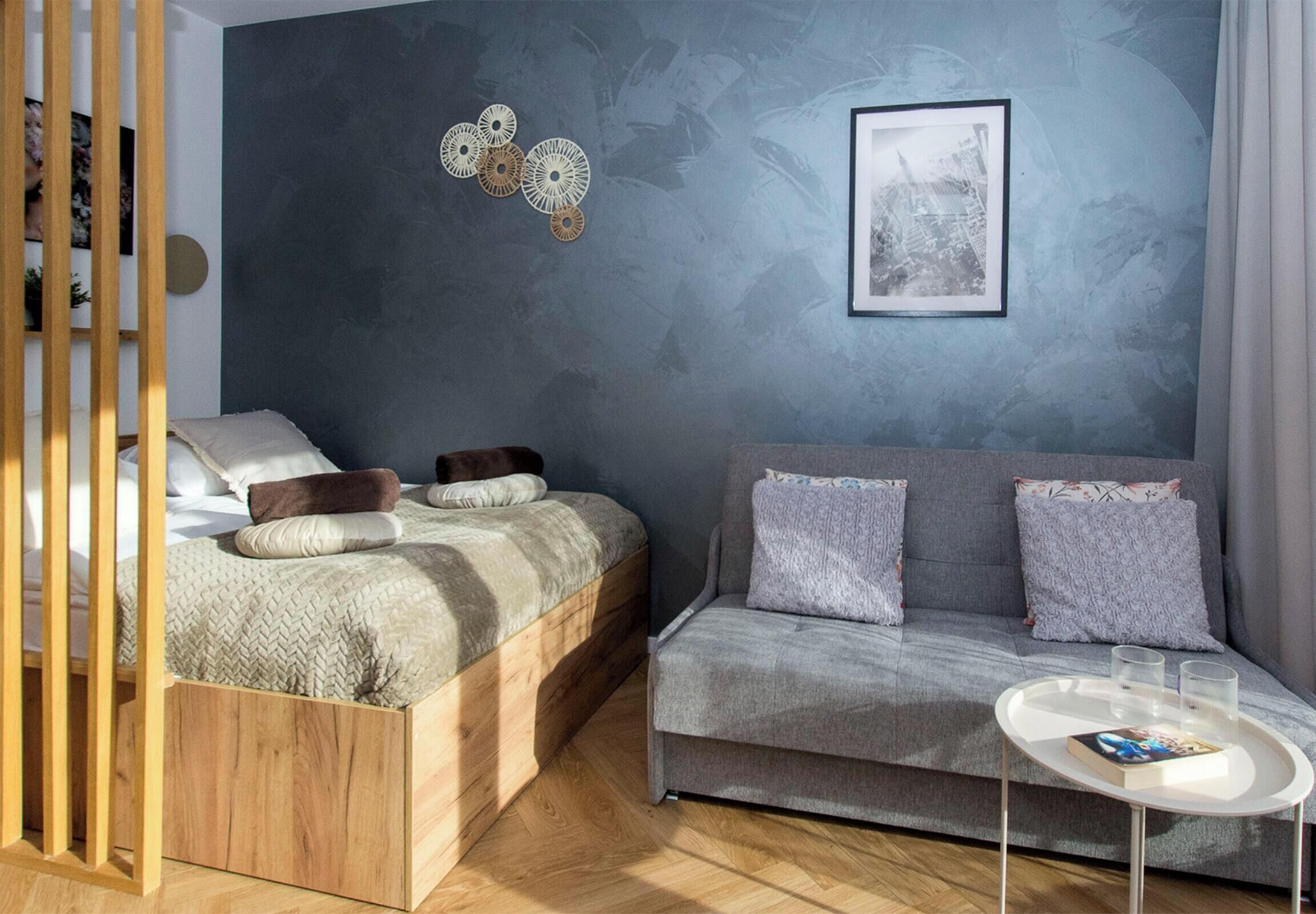 A modern bedroom with a bed, a sofa, a small table, and a wall-mounted artwork.