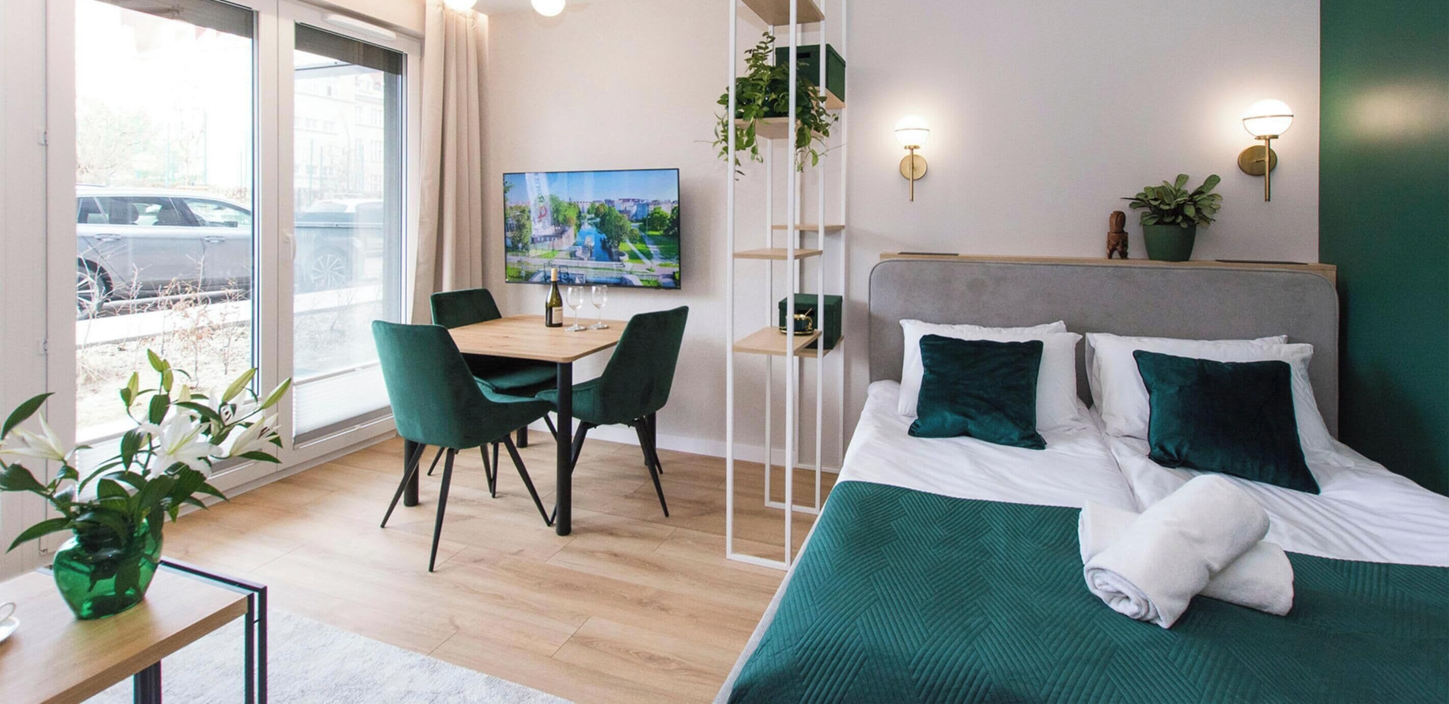 A hotel room with a bed, a desk with two chairs, a TV, and a balcony with a view of the street.