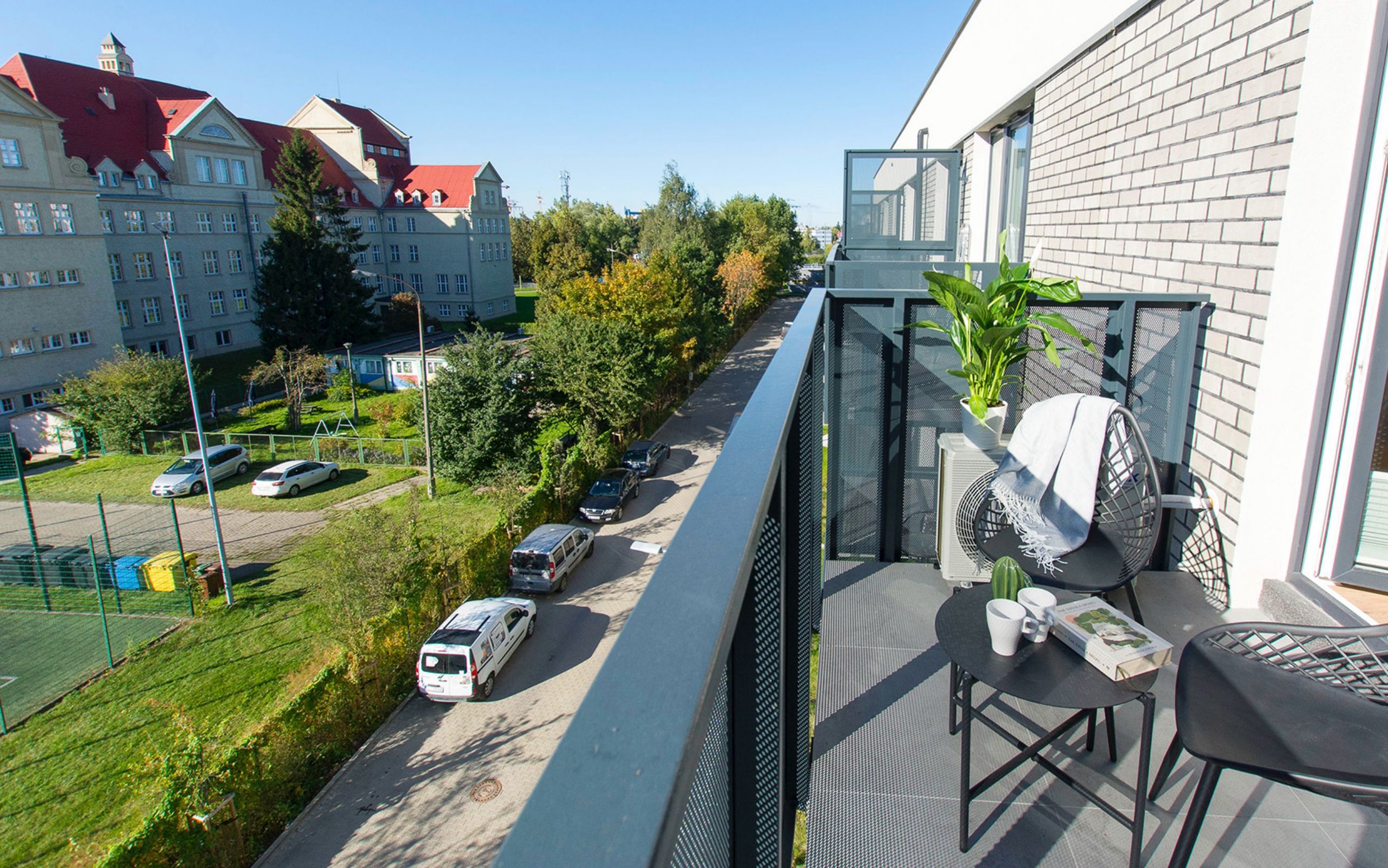 A balcony with a chair, a potted plant, and a table with a book and a cup.