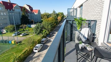 A balcony with a chair, a potted plant, and a table with a book and a cup.