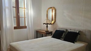 Ein Schlafzimmer mit einem Bett, einem Nachttisch, einem Spiegel und einem Fenster mit Vorhängen.