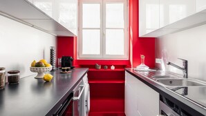 Une cuisine moderne avec des meubles blancs, un mur d’accent rouge, une fenêtre et un évier en acier inoxydable.