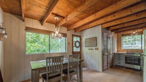 A rustic kitchen with wooden beams, a dining table with chairs, and a large window with a view of greenery. - Raven Ridge by Innsbrook Vacations! (Innsbrook)