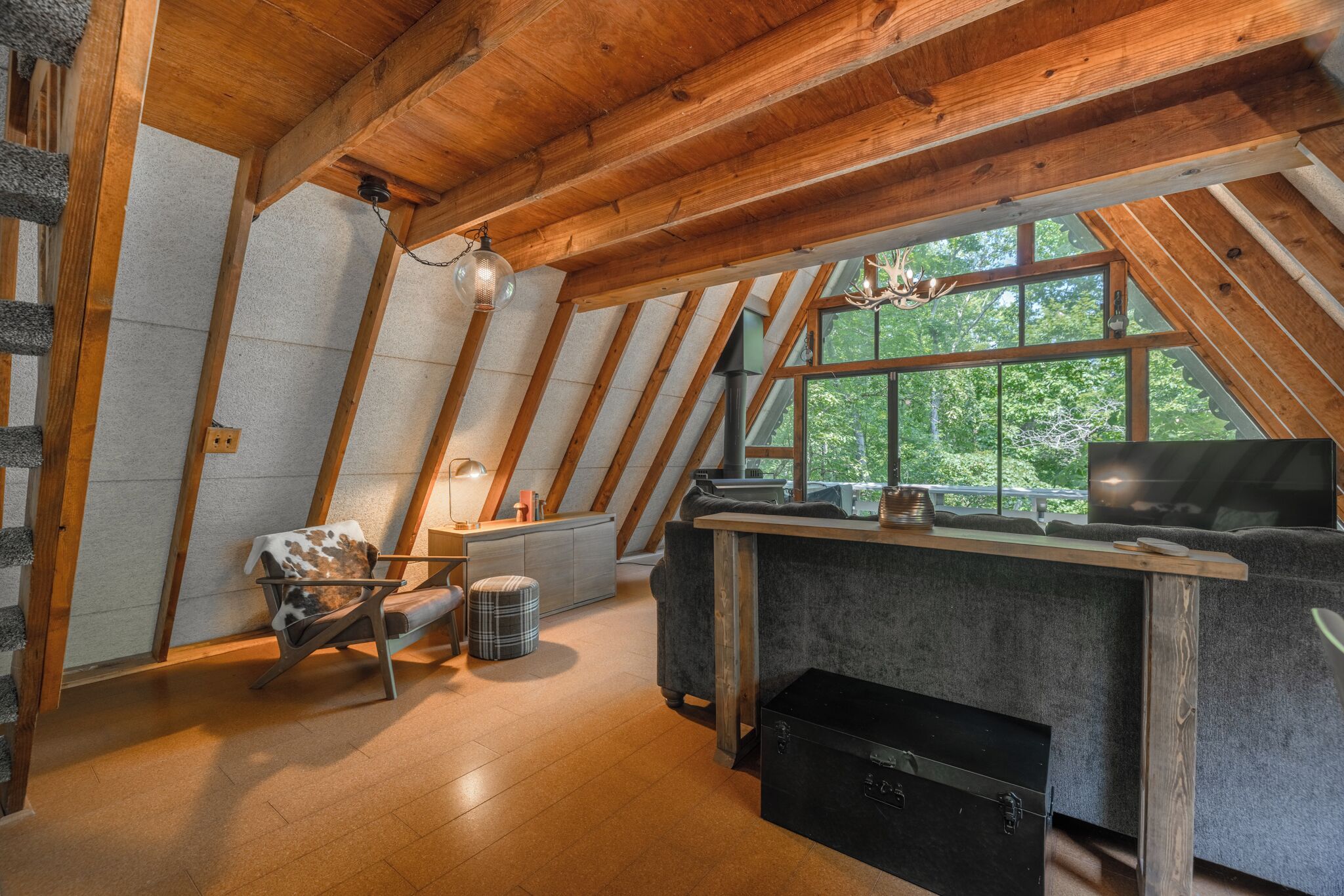 A cozy attic room with a sloped ceiling, a fireplace, a television, and a window overlooking greenery.