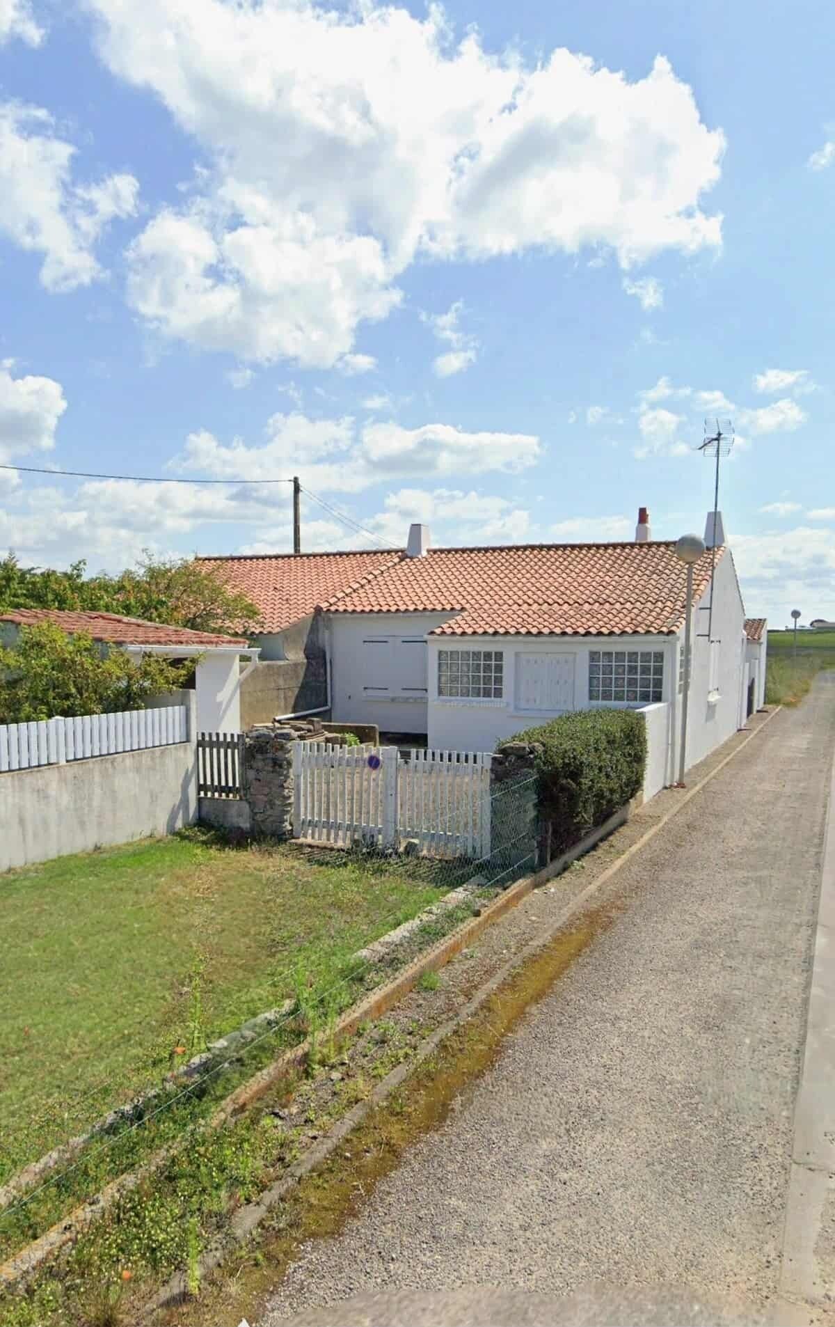 Une petite maison avec un toit en tuiles, une cour clôturée et une allée gravillonnée.
