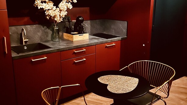 A compact kitchen with red cabinetry, a black countertop, a sink, and a small dining area with two chairs and a table. - La traversière the secrets of desire (Villeneuve-sur-Lot)