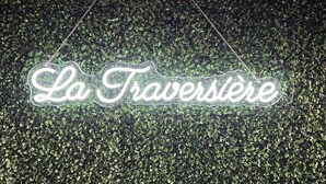 A neon sign with the text "La Traversière" against a backdrop of green foliage. - La traversière the secrets of desire (Villeneuve-sur-Lot)