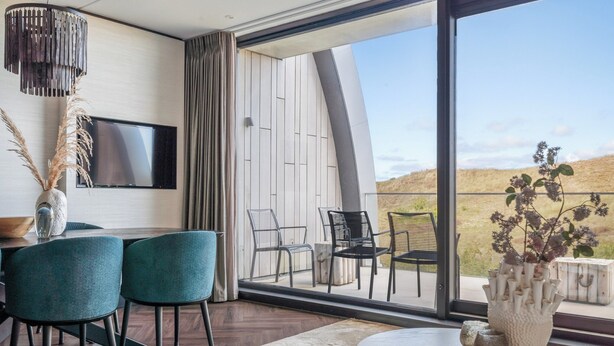 Una sala de estar moderna con un gran ventanal, un televisor de pantalla plana y un comedor con sillas y una mesa.